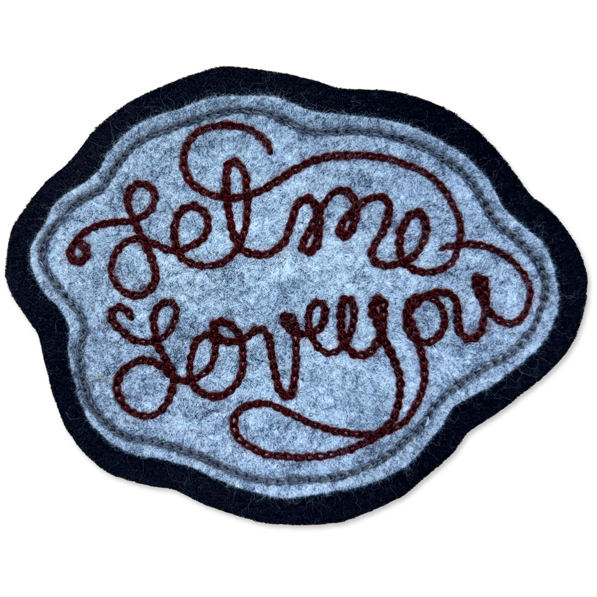 A felt patch with the phrase 'Let me love you' in dark brown cursive lettering, featuring a textured light blue center, a dark navy blue border, and a thin light blue inner border, shown on a plain white background.